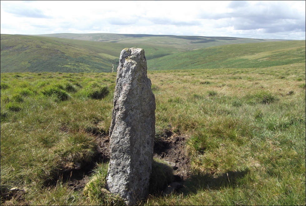 A granite standing stone on a hilltop with Stall moor beyond on a sunny summer day.